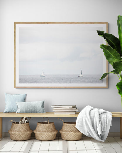 Minimalist ocean print featuring two sailboats on a calm ocean under a vast, bright sky. This serene seascape is ideal for coastal, nautical theme wall art. Photograph in minimalist mock up